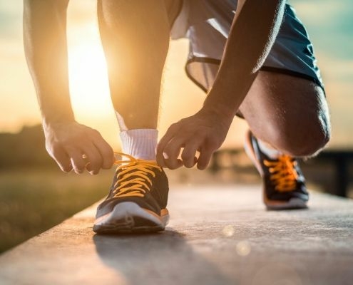 Image of runner tying their shoes as the sun rises. Use our blog's holiday training tips to stay on track for 3M Half Marathon.