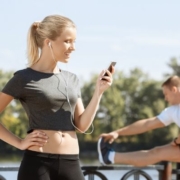 Image of female runner setting her running playlist while a male runner stretches. This 3M Half Marathon blog showcases 10 new songs for a running playlist update.