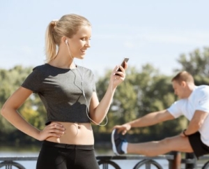 Image of female runner setting her running playlist while a male runner stretches. This 3M Half Marathon blog showcases 10 new songs for a running playlist update.