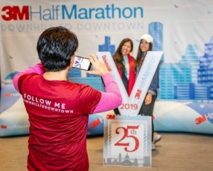 A 3M Half Marathon Ambassador takes a photo of two runners and the oversized 2019 3M Half Marathon medal at the 2019 3M Half Marathon expo. Take your photo with a giant 2020 3M Half Marathon medal, one of the many 2020 expo highlights.