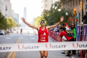Image of Philippe Rolly with hands in the air, about to cross a finish line. Rolly will run with the 2020 elite field at the 2020 3M Half Marathon presented by Under Armour.