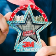 Image of two hands displaying the 26th annual 3M Half Marathon presented by Under Armour finisher medal.
