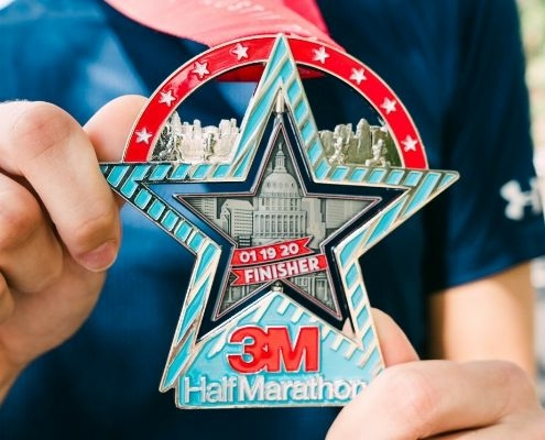 Image of two hands displaying the 26th annual 3M Half Marathon presented by Under Armour finisher medal.