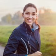 Image of runner listening to her headphones while smiling before a run. This blog has January running playlist additions for our #WeLiketheSoundofThat playlist.