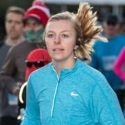 Picture of a young woman running the 2019 3M Half Marathon while listening to head phones. She'll add songs to her running playlist from this list of March running playlist additions!