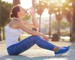 Image of woman drinking from a water bottle after a run. Proper hydration is an important self-care tip in this 3M Half Marathon blog.