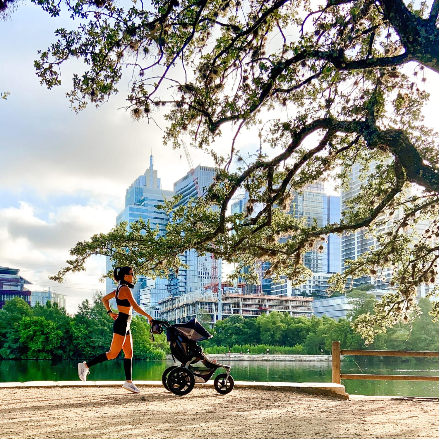 Image of Samantha, a runner and a mother, running with a stroller on the Town Lake Trail with the Austin skyline in the background. She contributed some of the information in this blog about how to run with a stroller.